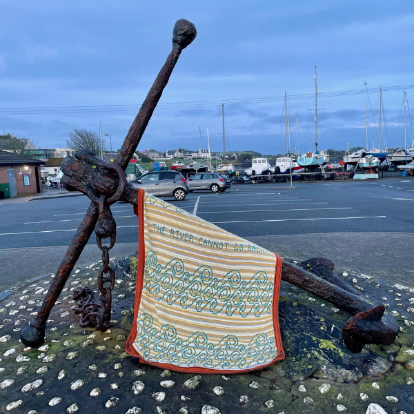 Photo of a crocheted blanket on the sea coast laid on an anchor